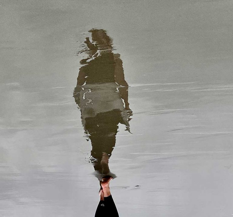 Schatten einer Frau spiegelt sich im rücklaufenden Wasser am Strand